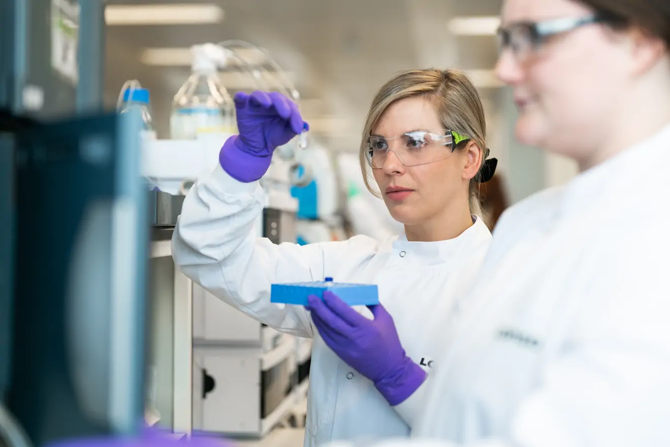 a scientist holds a small vial up to inspect it